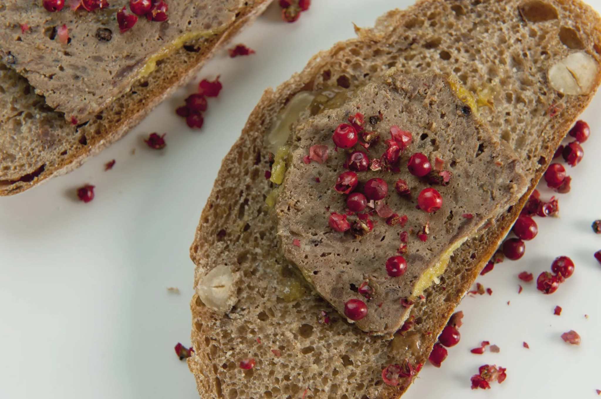 Close-up of terrine de canard topped with pink peppercorns on rustic bread slices